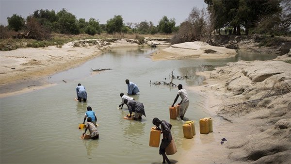 Persone che raccolgono acqua in taniche in un corso d'acqua quasi asciutto